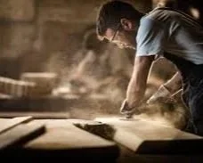 Un homme travaillant dans un atelier, manipulant du bois avec de la poussière en suspension.