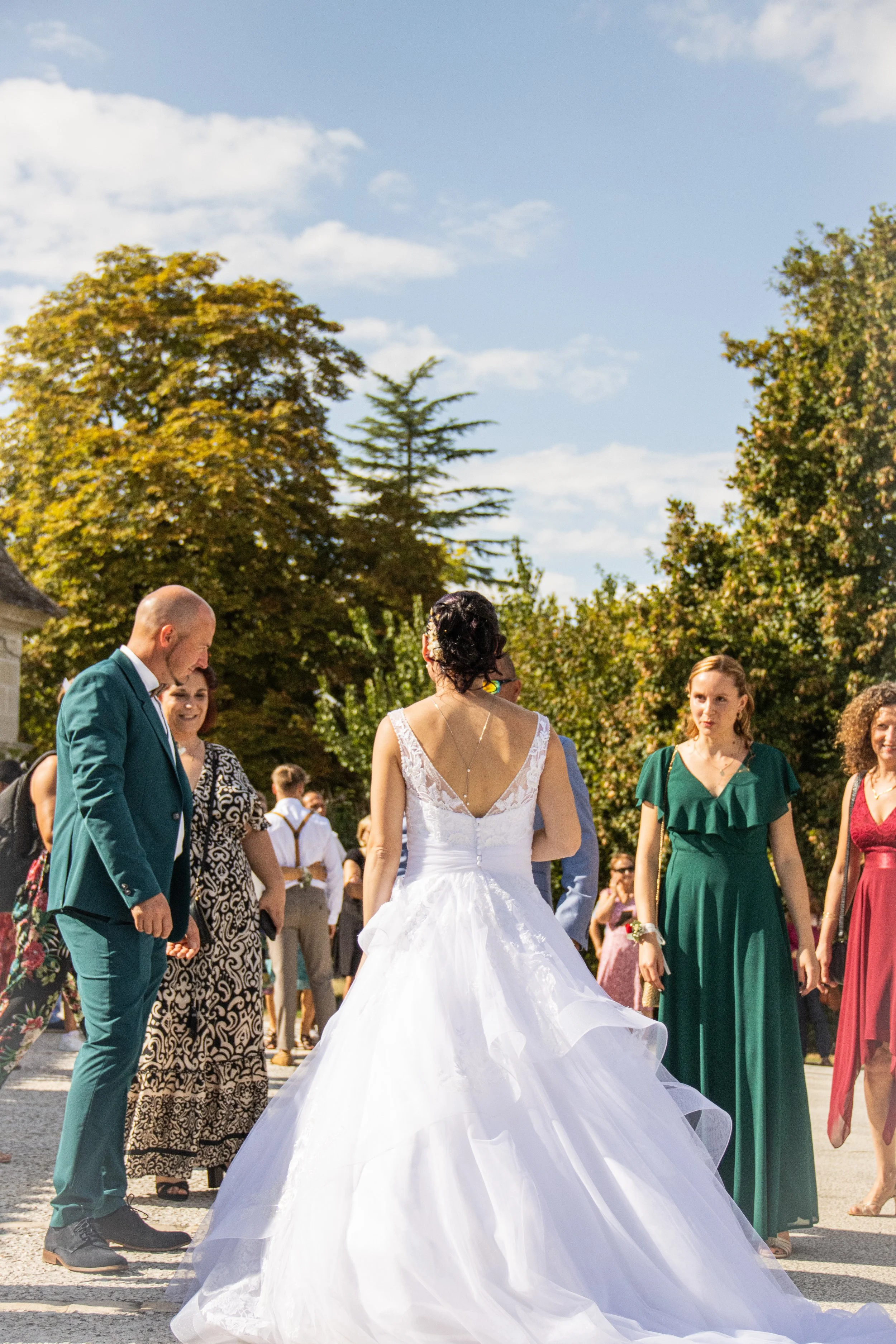 Femme en robe de mariée blanche entourée de personnes lors d'une cérémonie en plein air sous un ciel ensoleillé.