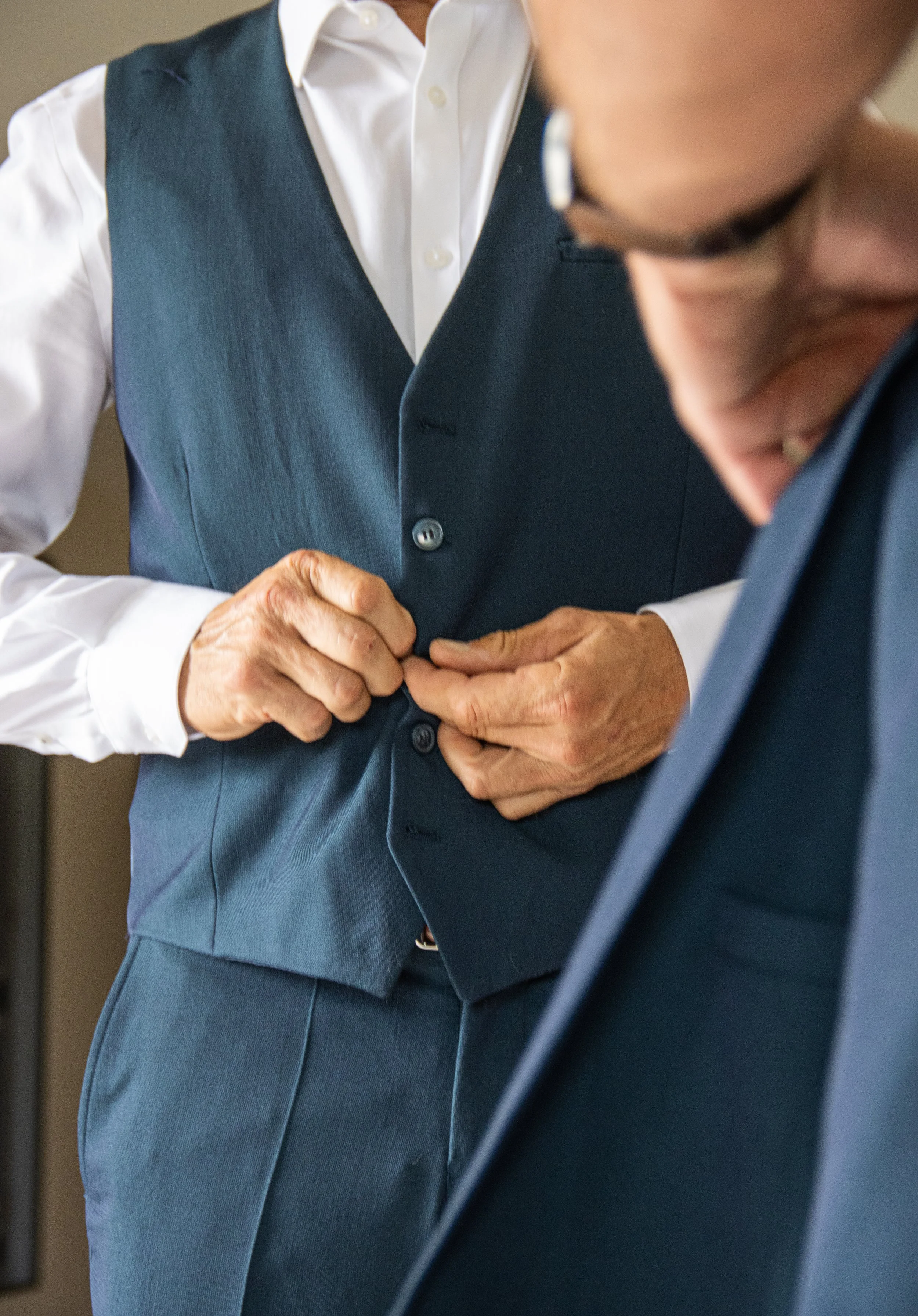 Deux hommes en costume se préparent, l'un ajuste le bouton de son veston.