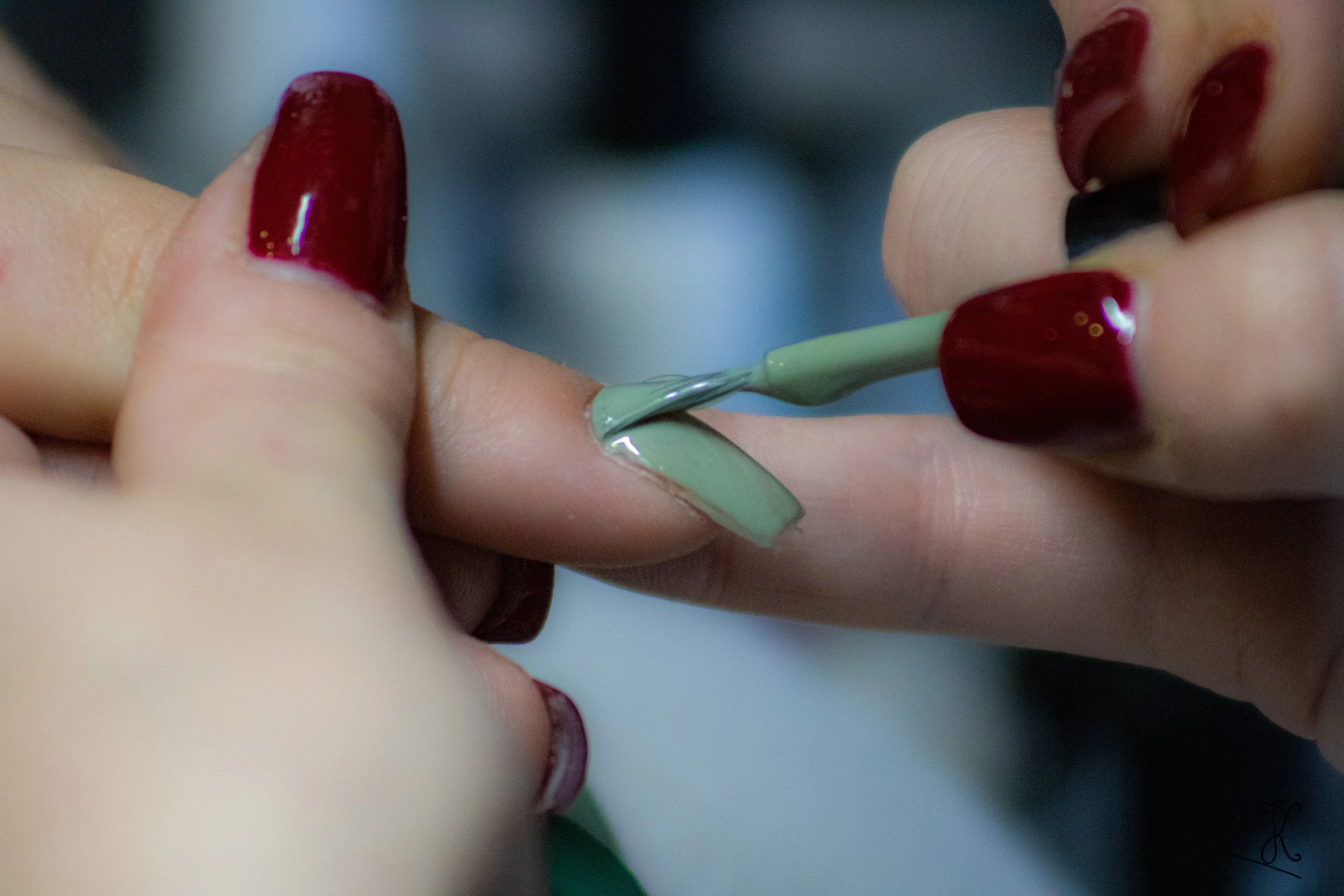 Une personne applique du vernis à ongles vert sur un doigt, avec d'autres doigts déjà vernis en rouge.