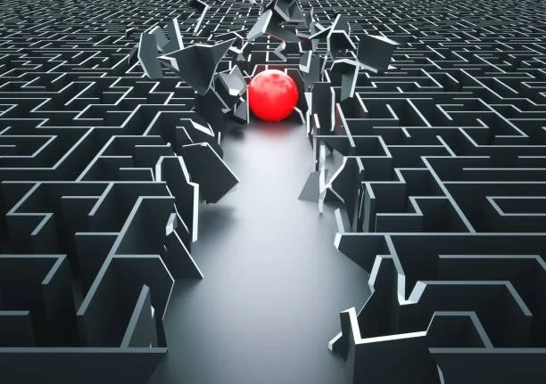 A maze with black walls and white pathways, featuring a red sphere at the center surrounded by broken walls.