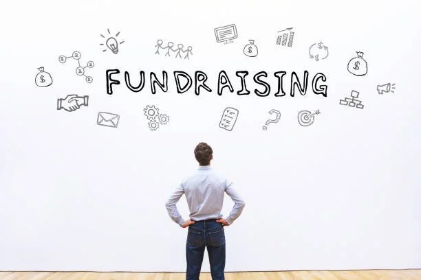 A man standing with hands on hips looking at a wall with the word 'FUNDRAISING' and various related icons drawn around it.