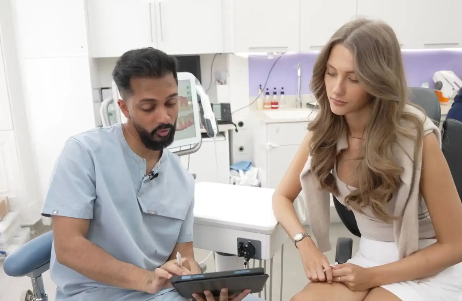 Doctor consulting with a female patient in a medical office with medical equipment and monitors in the background.