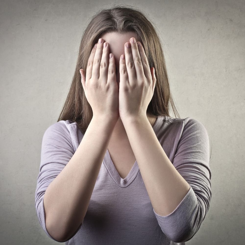 Frau mit langem braunem Haar bedeckt Gesicht mit beiden Händen.