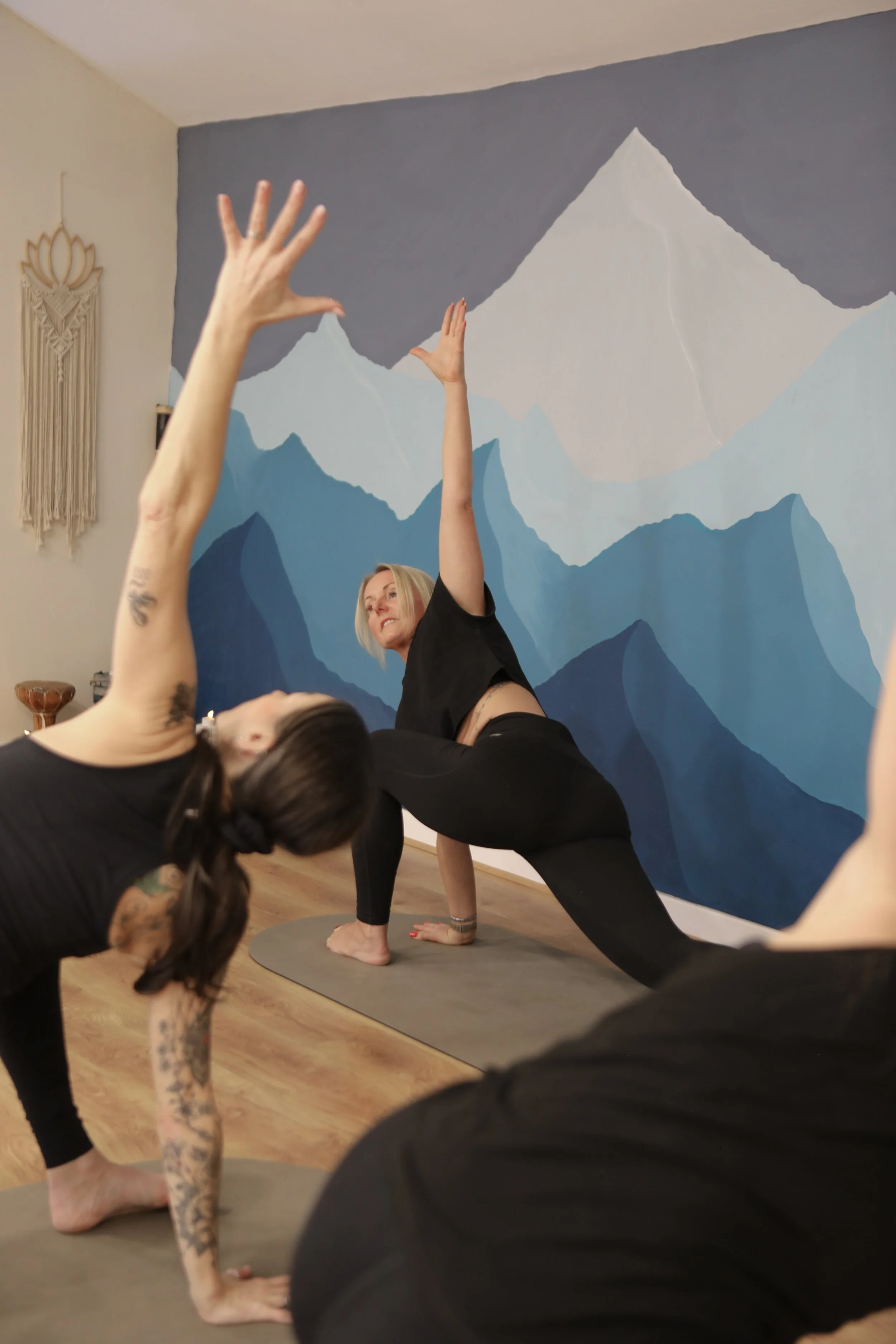 Group of people practicing yoga in a studio with green and red lighting, using mats and bolsters for support.