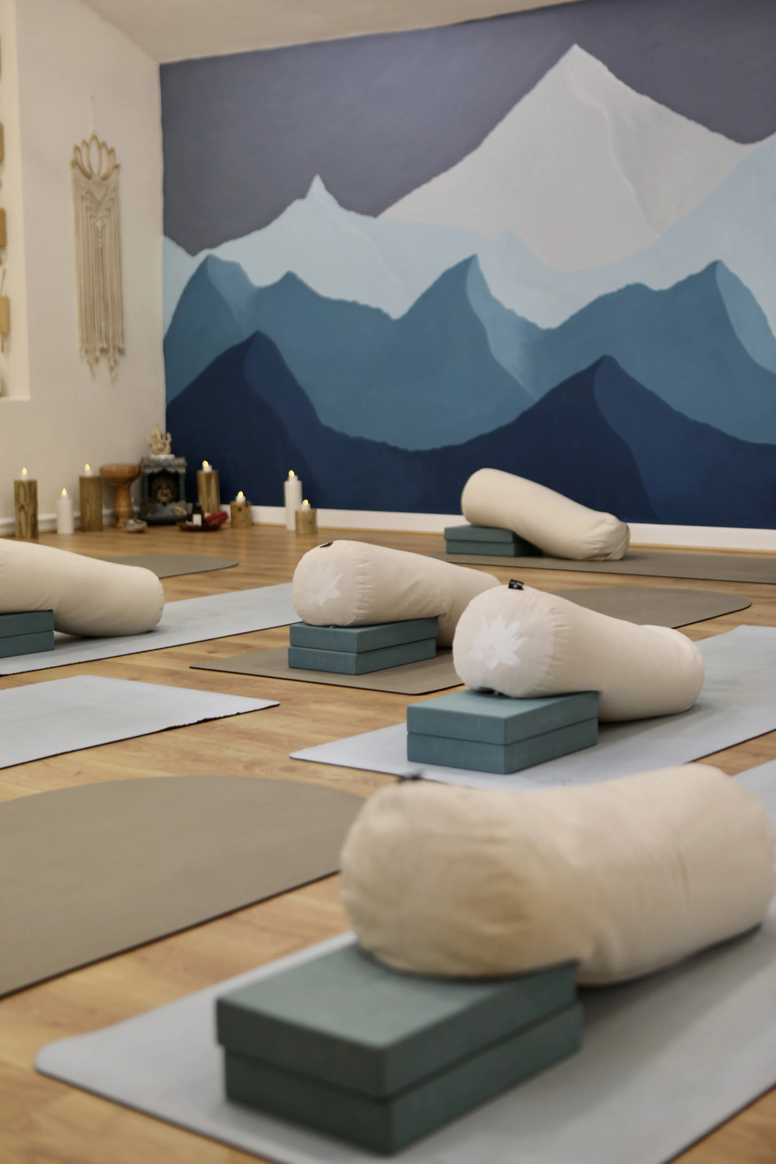 A yoga studio with rolled-up mats on rectangular blocks, in front of a mural of mountain peaks painted in shades of blue and gray.