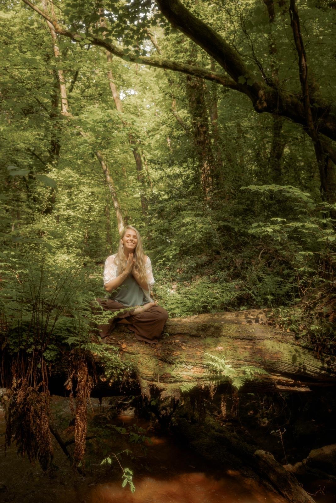 A woman practicing meditation on a fallen tree trunk in a dense, green forest.