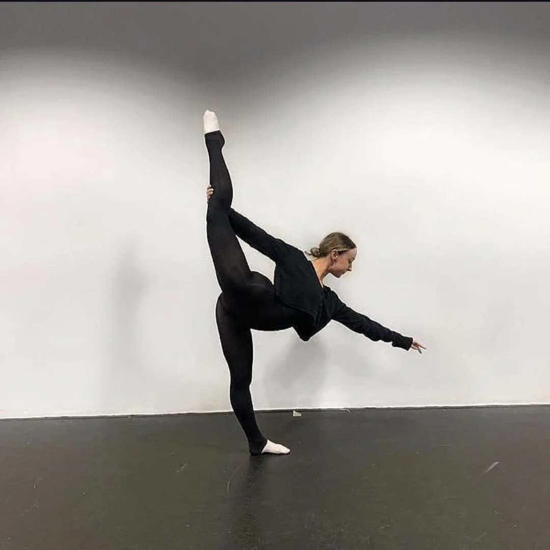 A woman performing a yoga pose where she balances on one leg, extends her other leg upward, and stretches her arms forward.