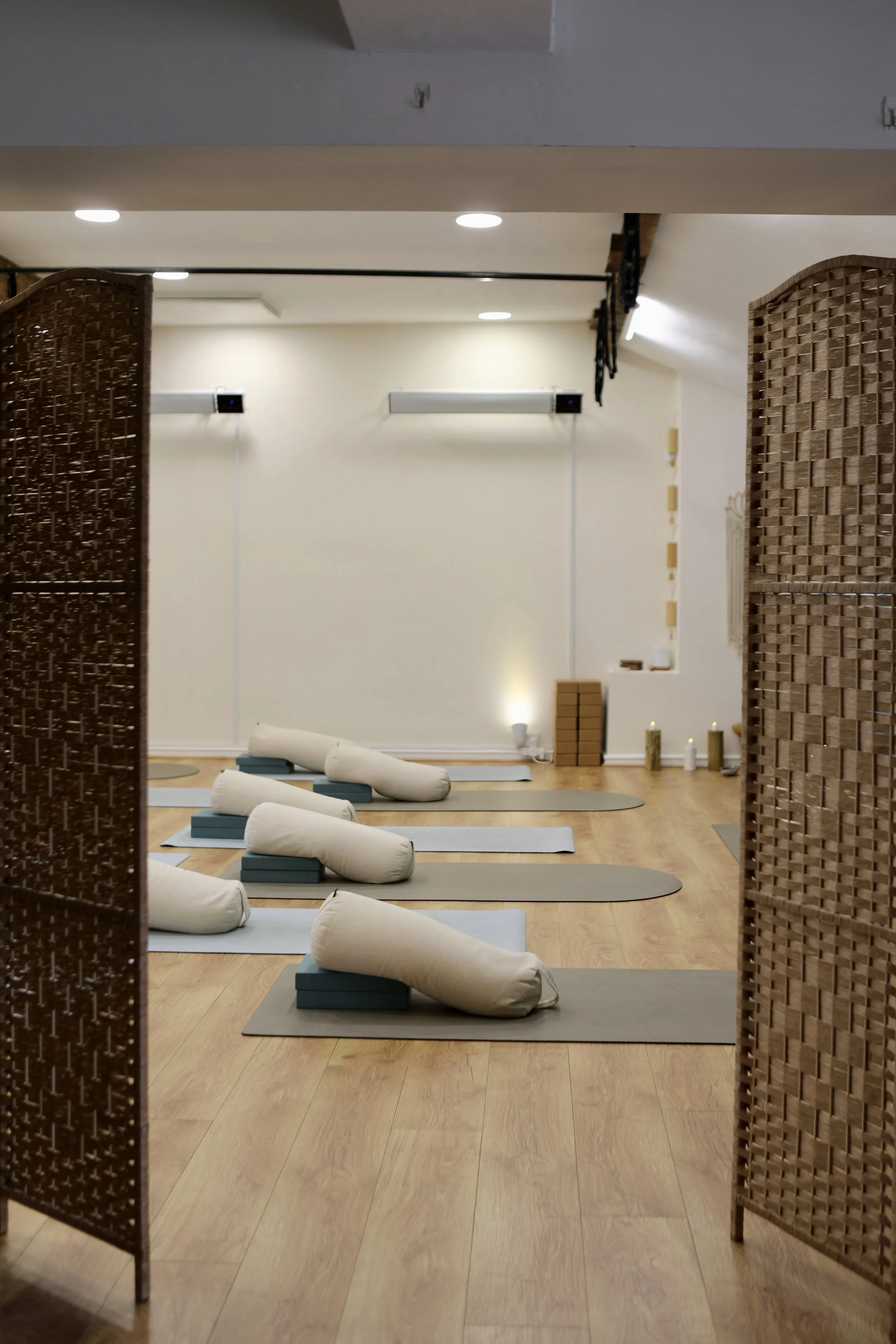 Yoga studio with mats, bolsters, and legs in a relaxing atmosphere, separated by woven chairs.