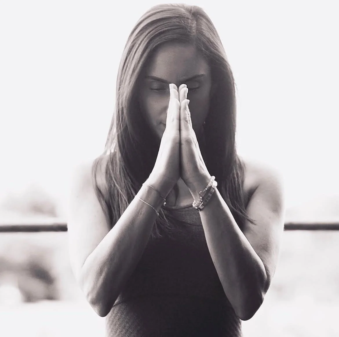 A woman with long hair praying with her hands pressed together in front of her face, eyes closed, in a black and white photo.