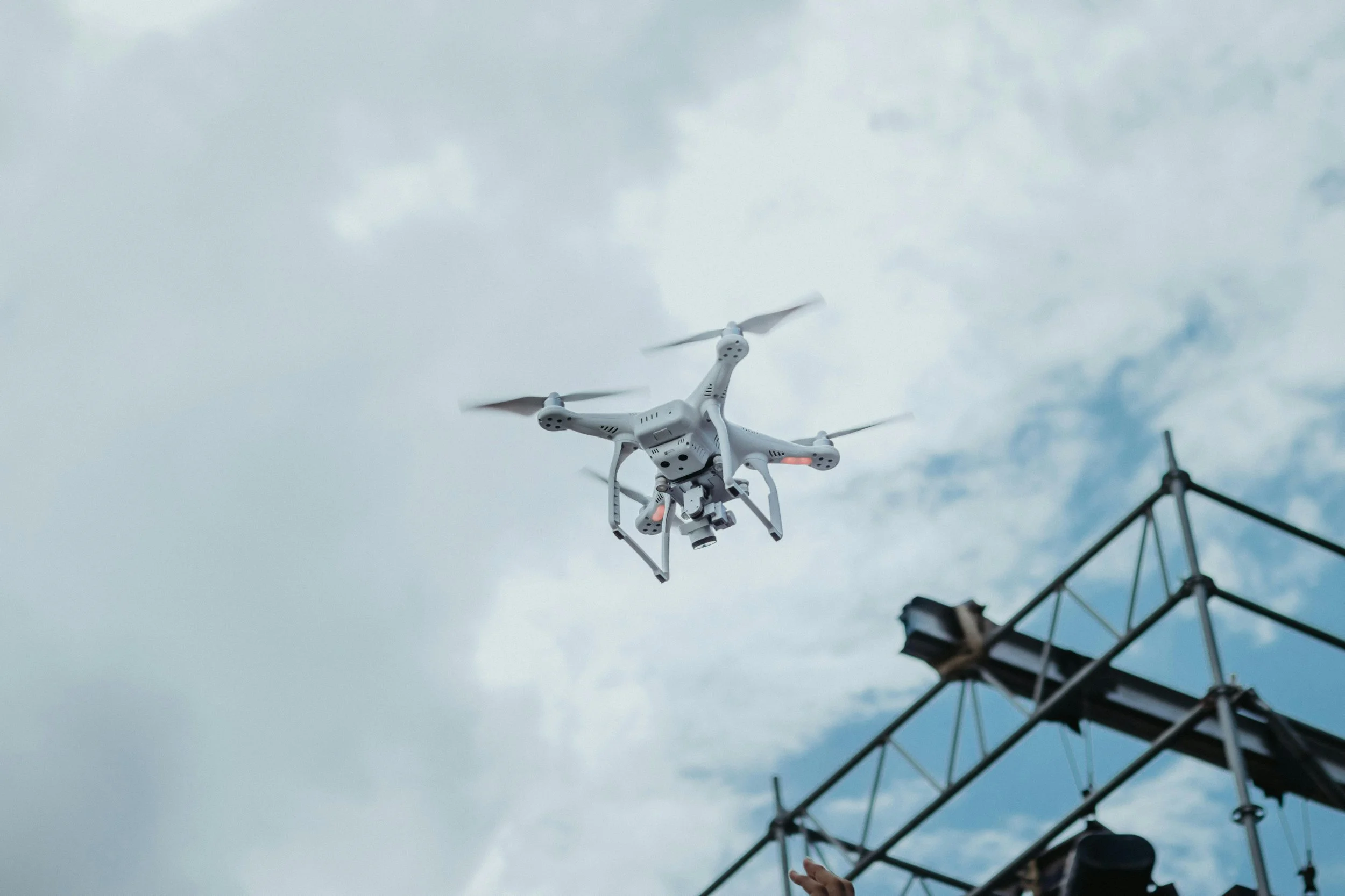 A drone flying over scaffolding on a roof on a cloudy day.