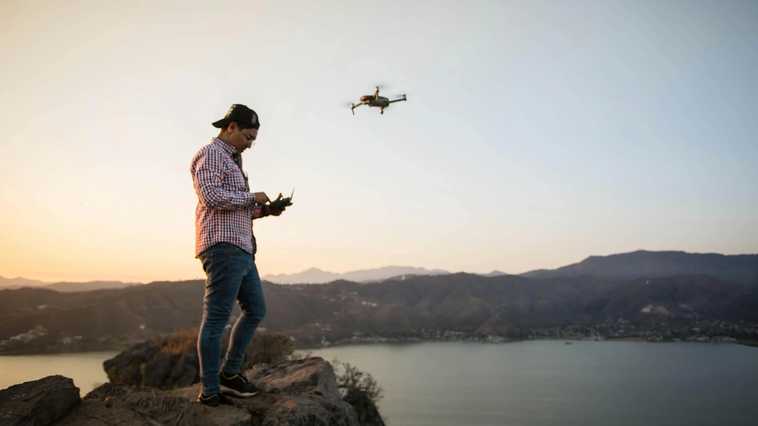 A man flying a drone over a scenic backdrop of an expanse of water and mountains.