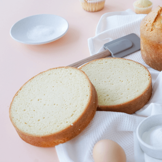 Sliced plain pound cake on a white cloth with baking tools and ingredients in the background.