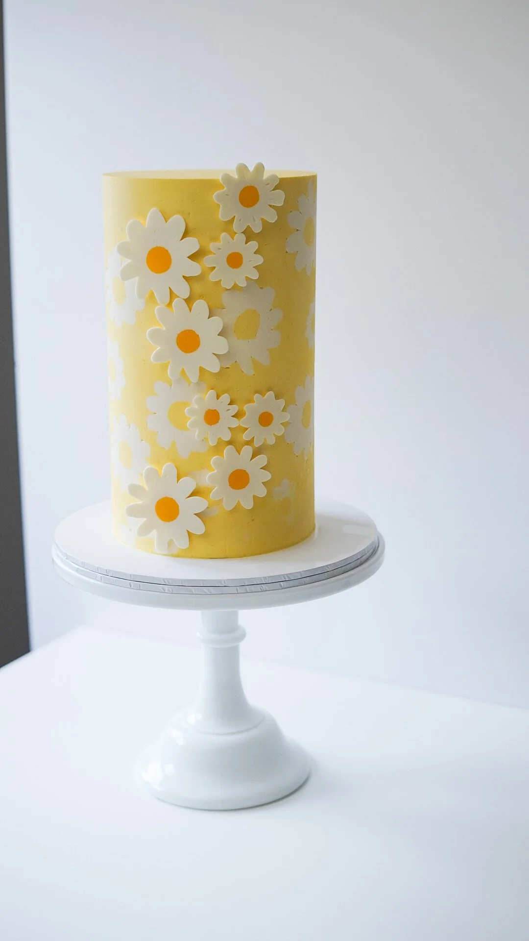 Yellow cake with white flower decorations on a white cake stand.