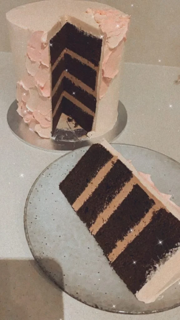 A slice of layered chocolate and cream cake on a glass plate and the remaining cake on a serving platter in the background.
