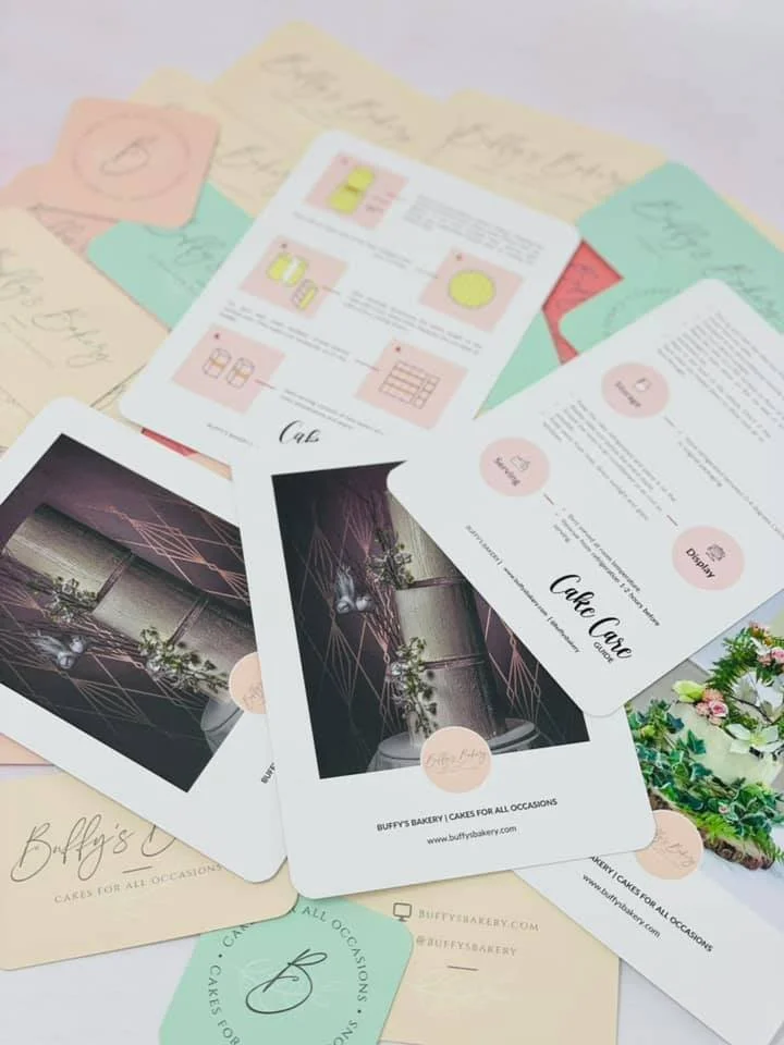 Flat lay of marketing materials for Buffy’s Bakery, including postcards, flyers, and a small cake display with flowers and greenery.