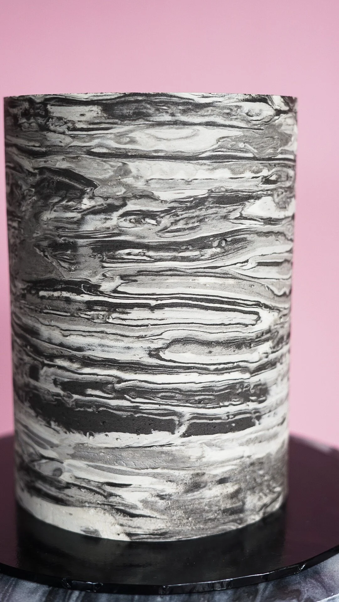 A cylindrical object with a black and white marbled pattern on a black base, set against a pink background.