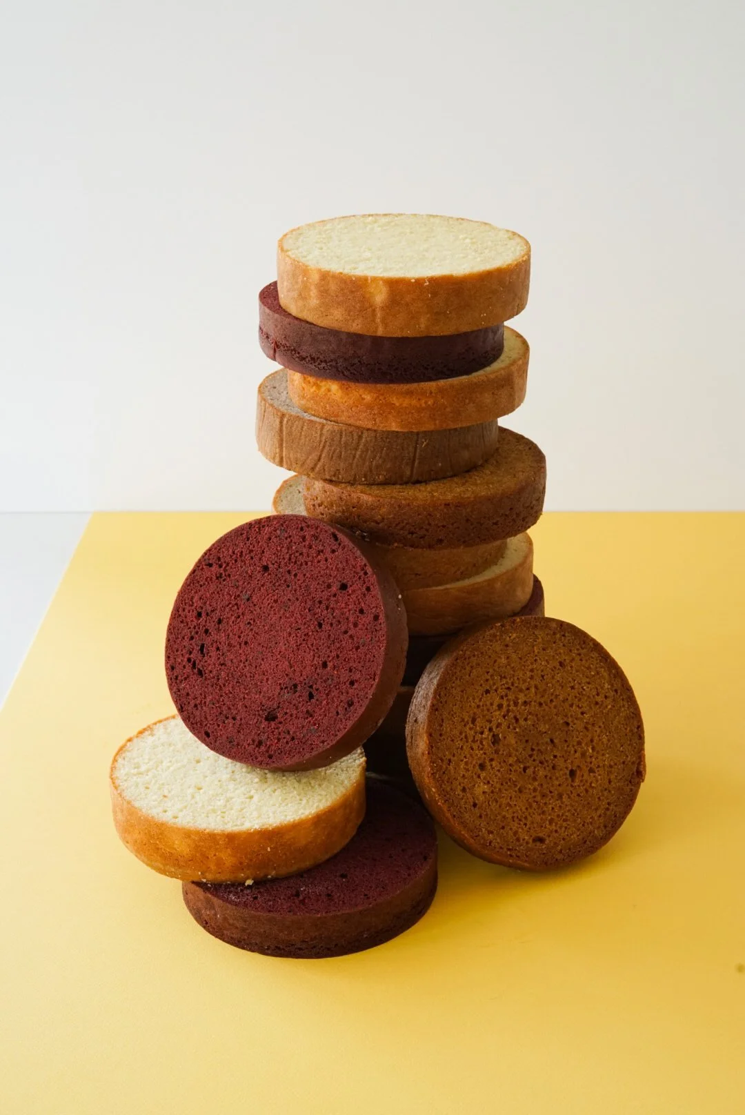 Colorful stack of assorted bakery sponge cake slices on yellow surface with white background.