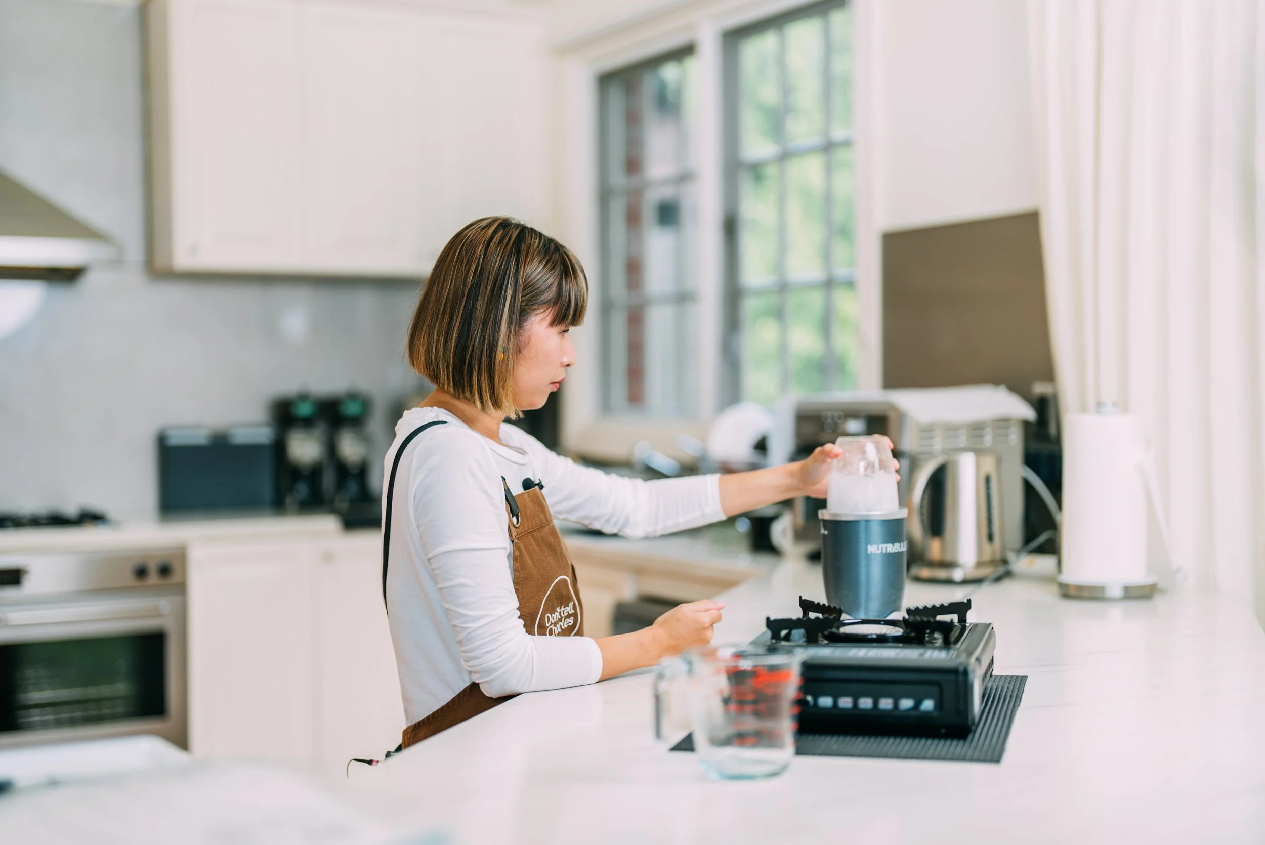 A woman in a kitchen using a NutriBullet blender to prepare a smoothie, with a measuring cup and kitchen appliances around her.