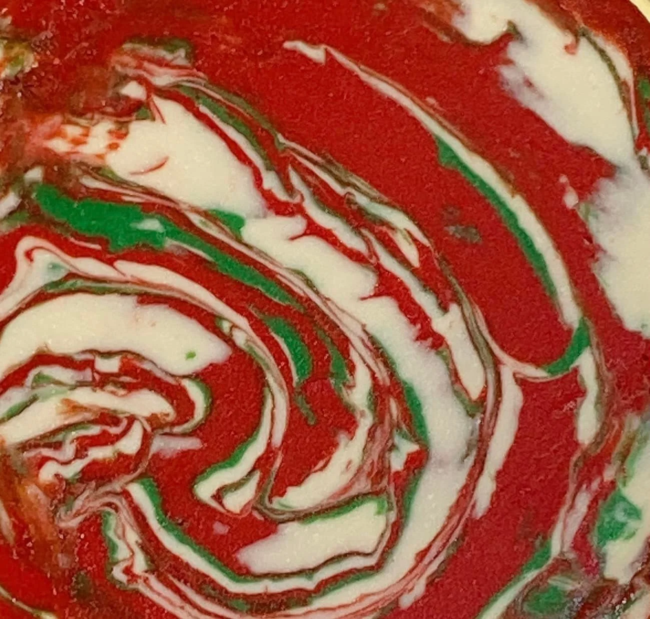 Close-up of a swirl pattern with red, green, white, and black colors, resembling a tie-dye or marbled design.