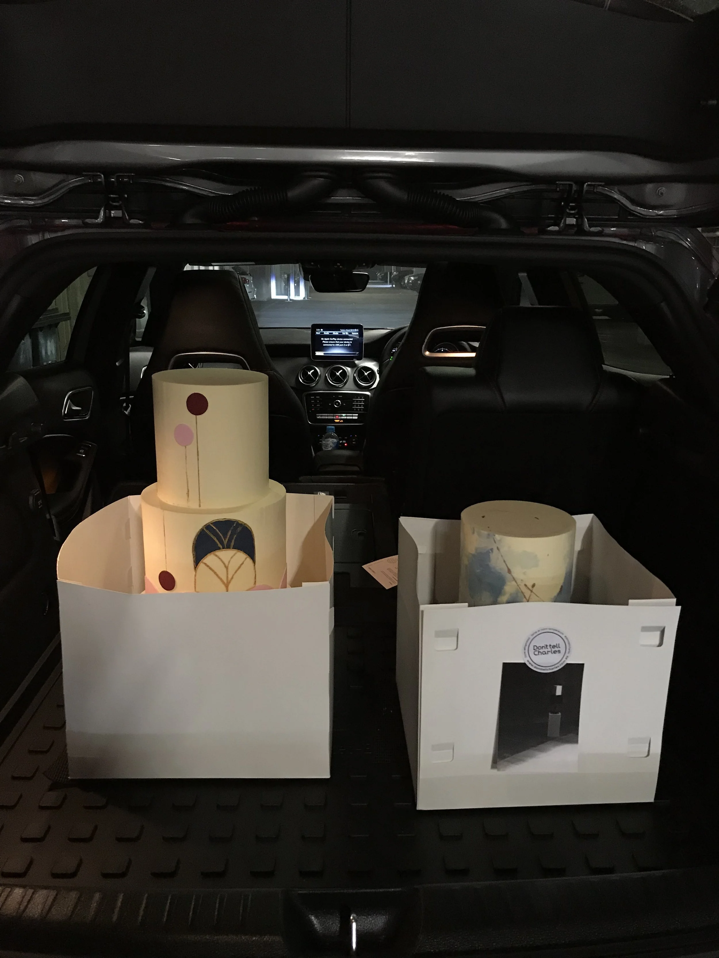Two boxed buttercream cakes secured in the boot of a car for delivery