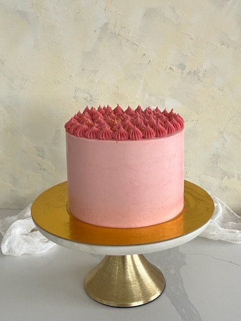 Pink frosted cake with piped swirls and golden star-shaped decorations on top, displayed on a gold cake stand.