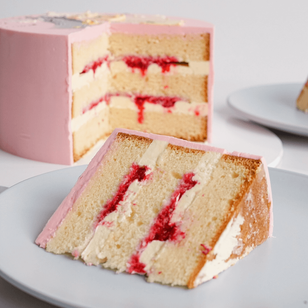 Slice of layered strawberry and cream cake on a white plate with remaining cake in the background.