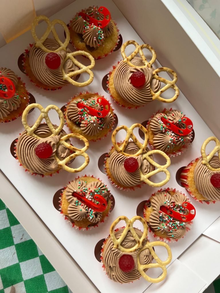 Assorted cupcakes with chocolate frosting, decorated with red cherries, colorful sprinkles, pretzels, and red and green candy decorations.