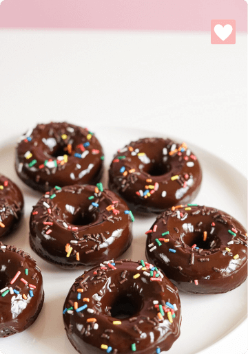 Chocolate-glazed donuts with colorful sprinkles on a white plate.