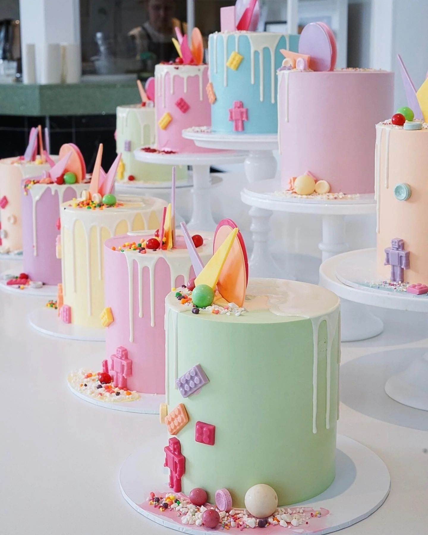Colorful, pastel-themed multi-layer cakes decorated with candy, sprinkles, and Lego-inspired decorations.