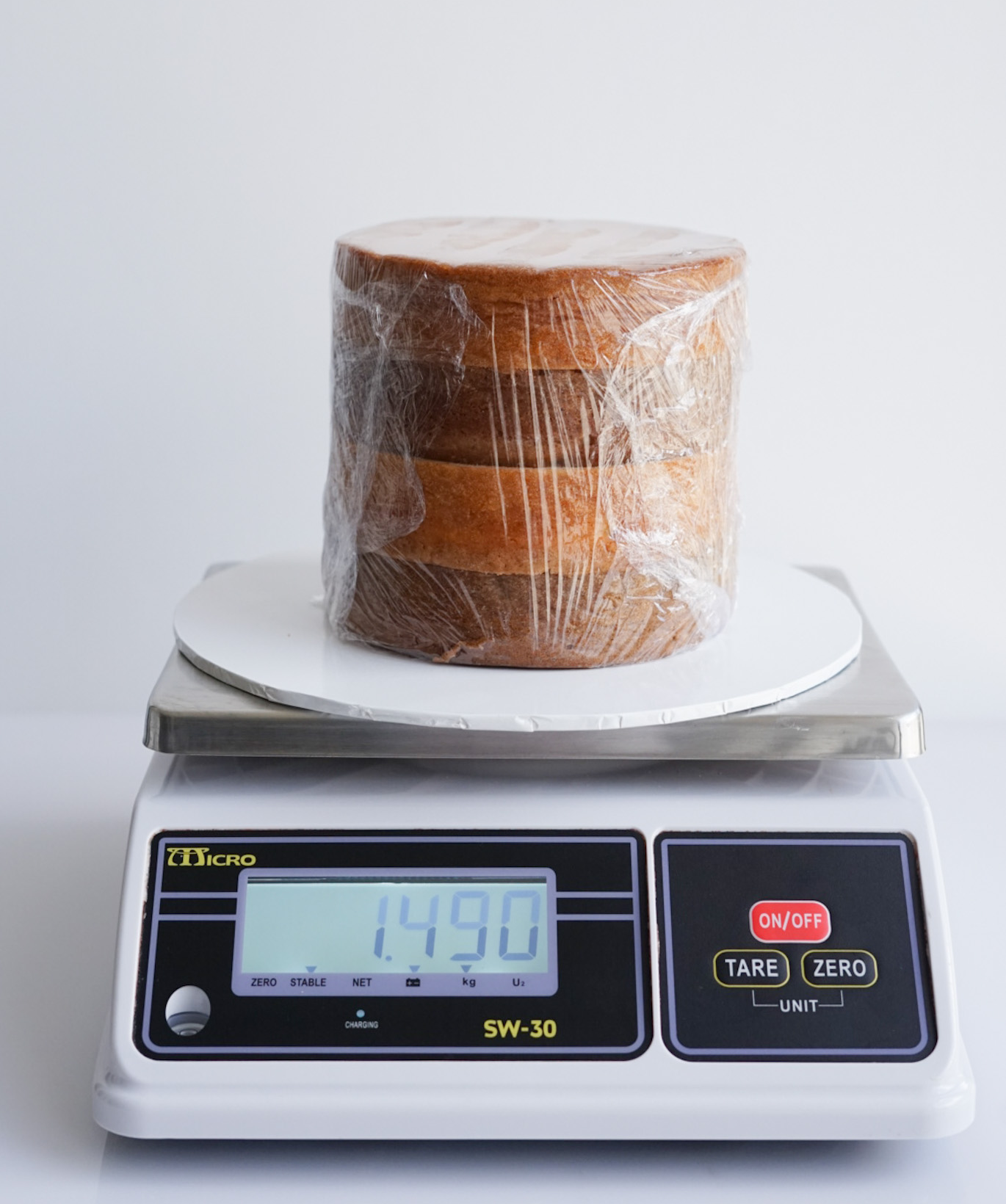 Cake layers and cake board on a kitchen scale to record Weight A before filling