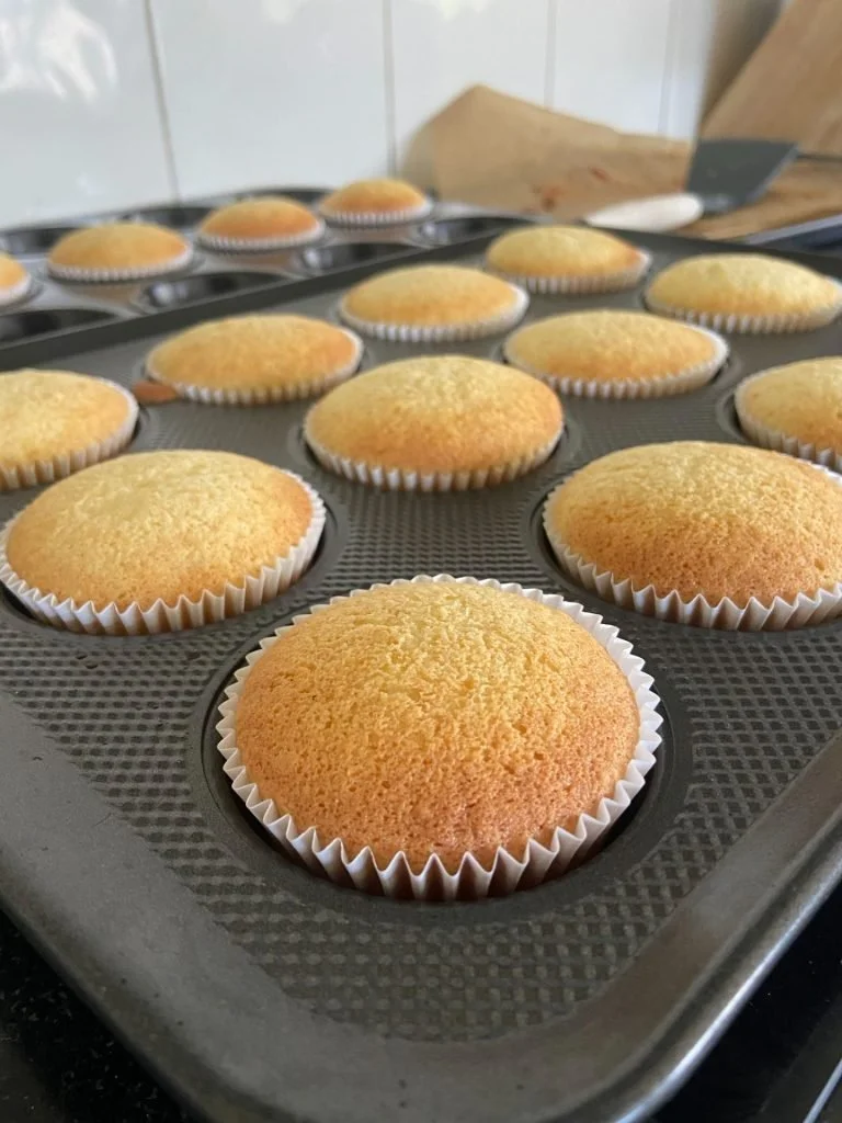 Freshly baked cupcakes on a baking sheet in a kitchen.