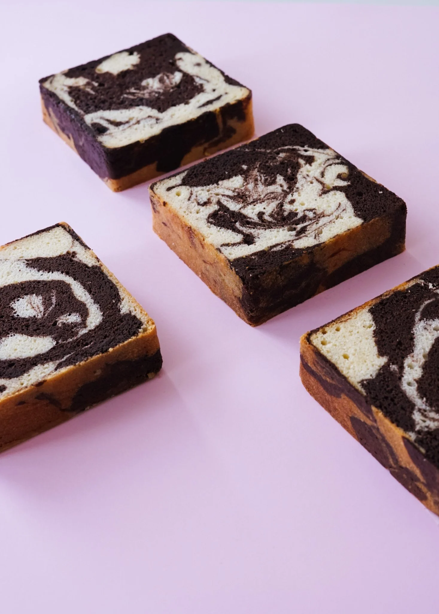 Four squares of marbled brownie with black and white swirls on a pink background.