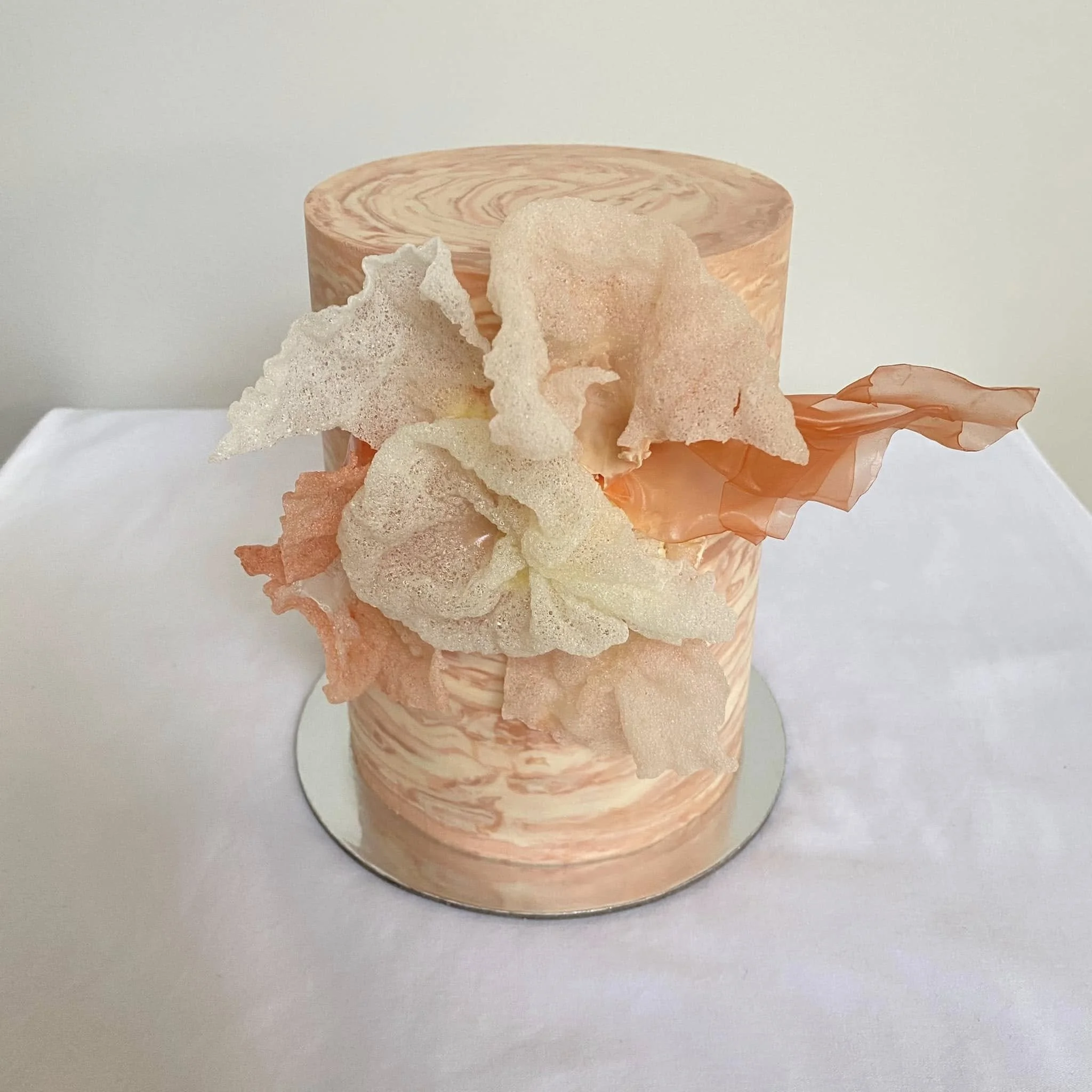 Round cake with pink and cream marbled icing topped with pink and white crispy rice treats and a pink tissue paper decoration.