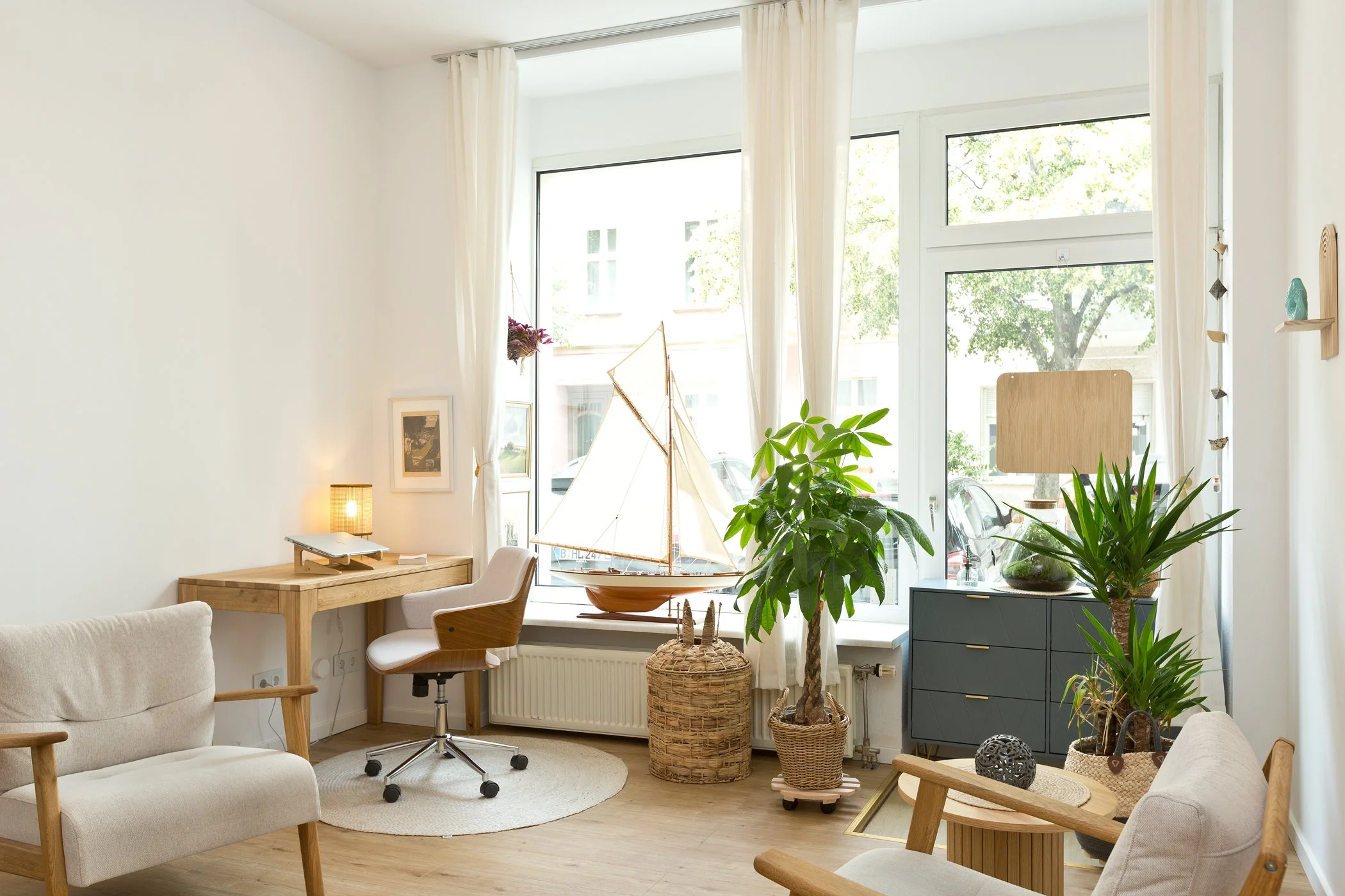 Heller Praxisraum mit weißen Sesseln, Schreibtisch und großem Fenster