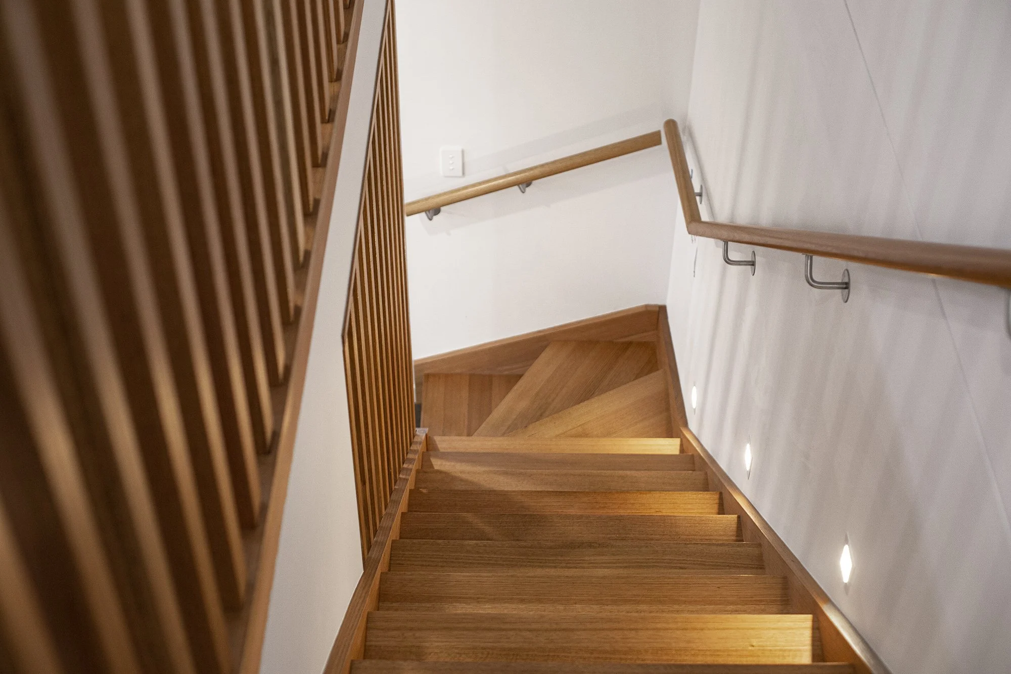 Wooden staircase with a handrail and wall-mounted lights, viewed from above.