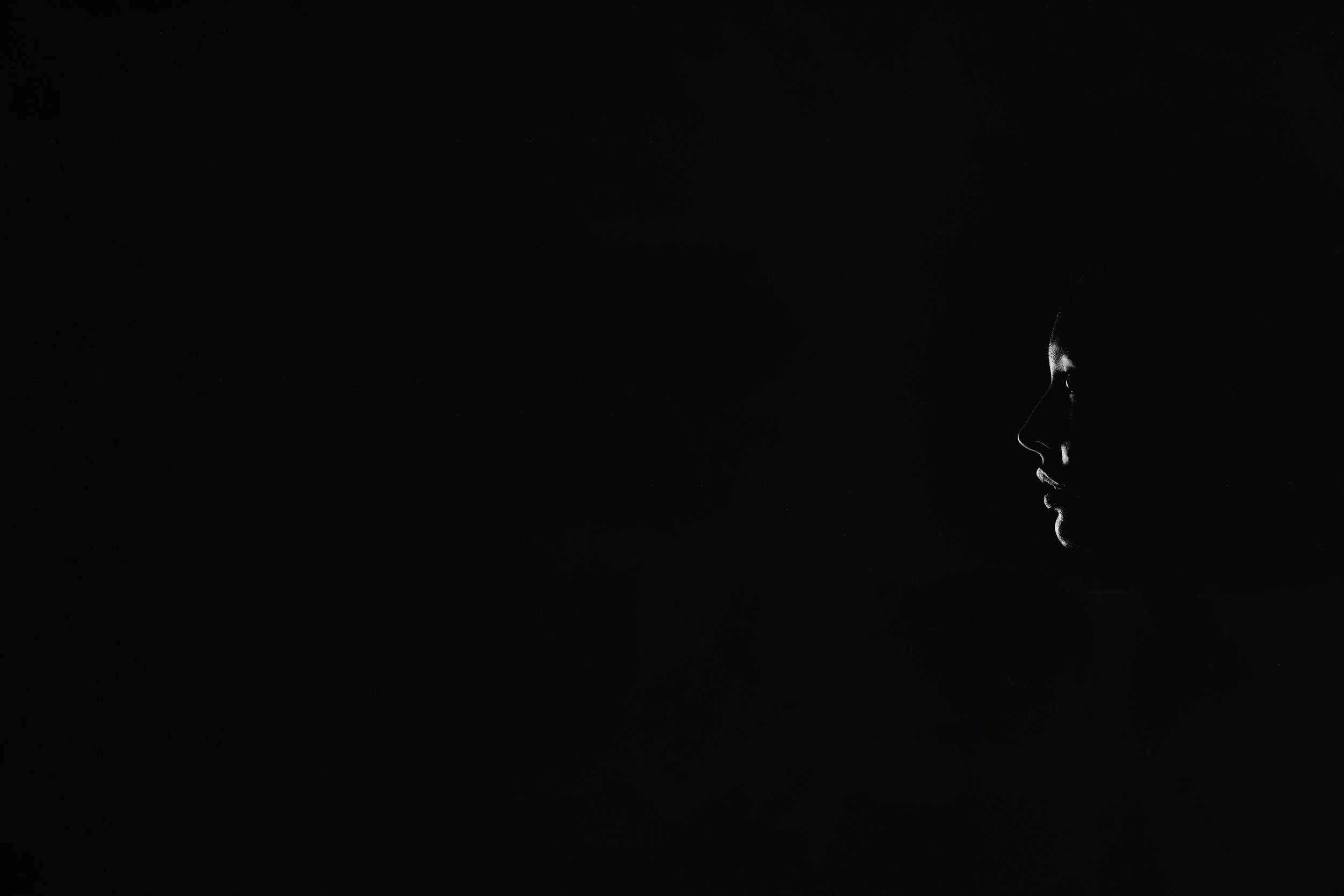 Silhouette of a person's face in profile against a dark background with minimal lighting highlighting facial features.
