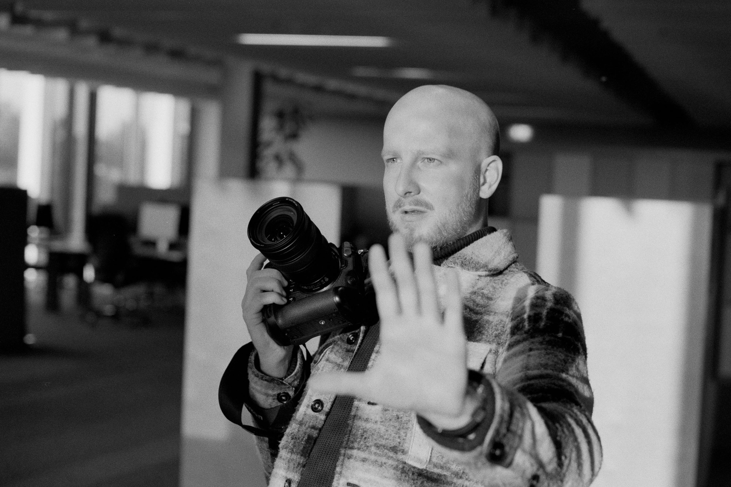 Black and white photo of a man holding a camera with his left hand raised as if signaling to stop