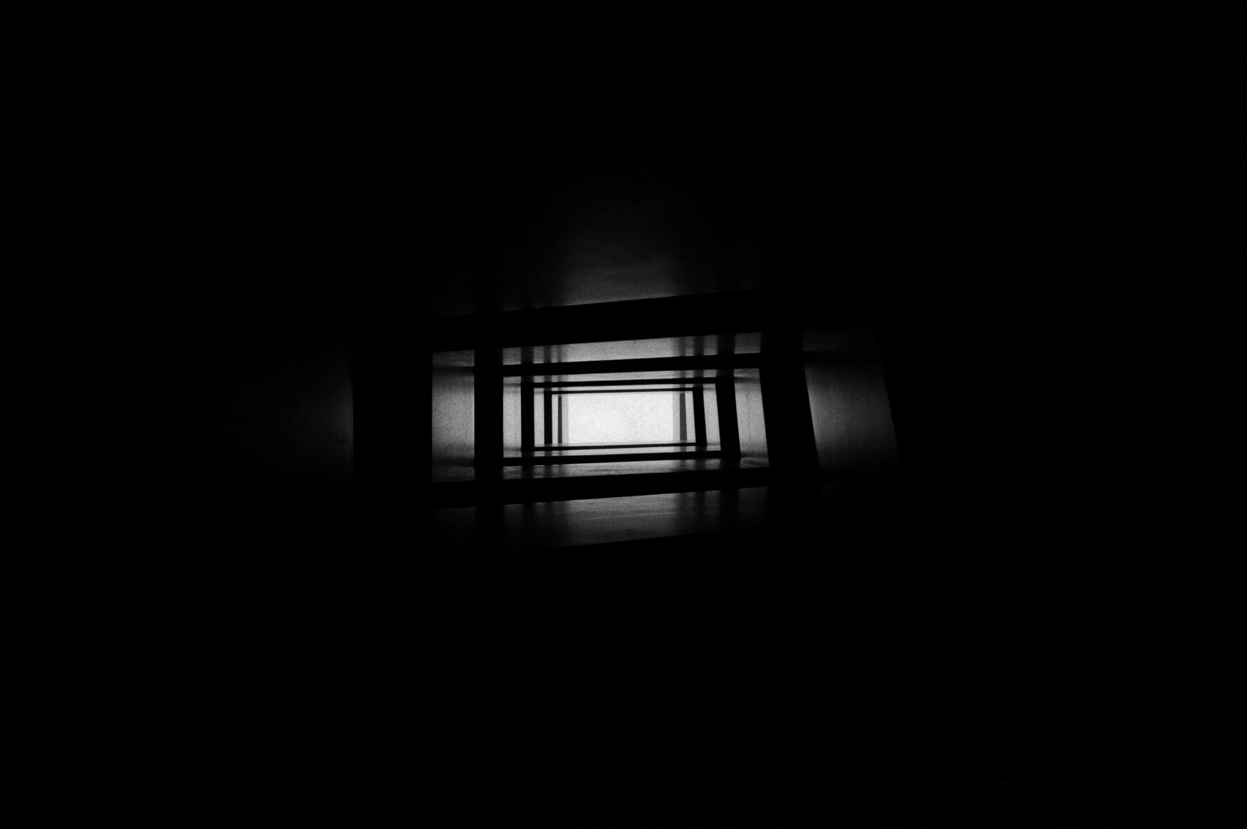 Black and white photo of a staircase viewed from the bottom, looking up towards the light at the top.