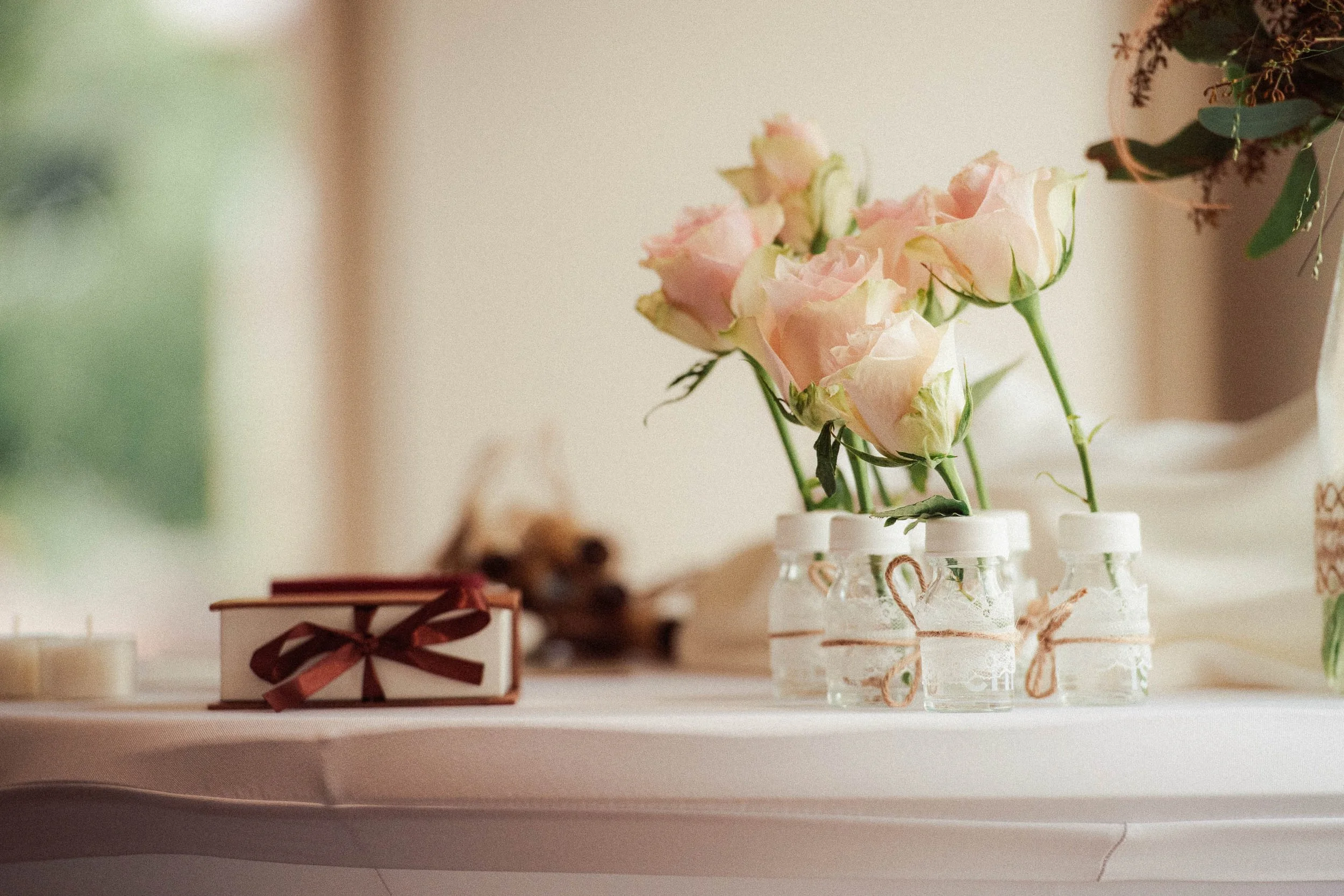 Pink and white roses in small glass jars decorated with twine on a white table.