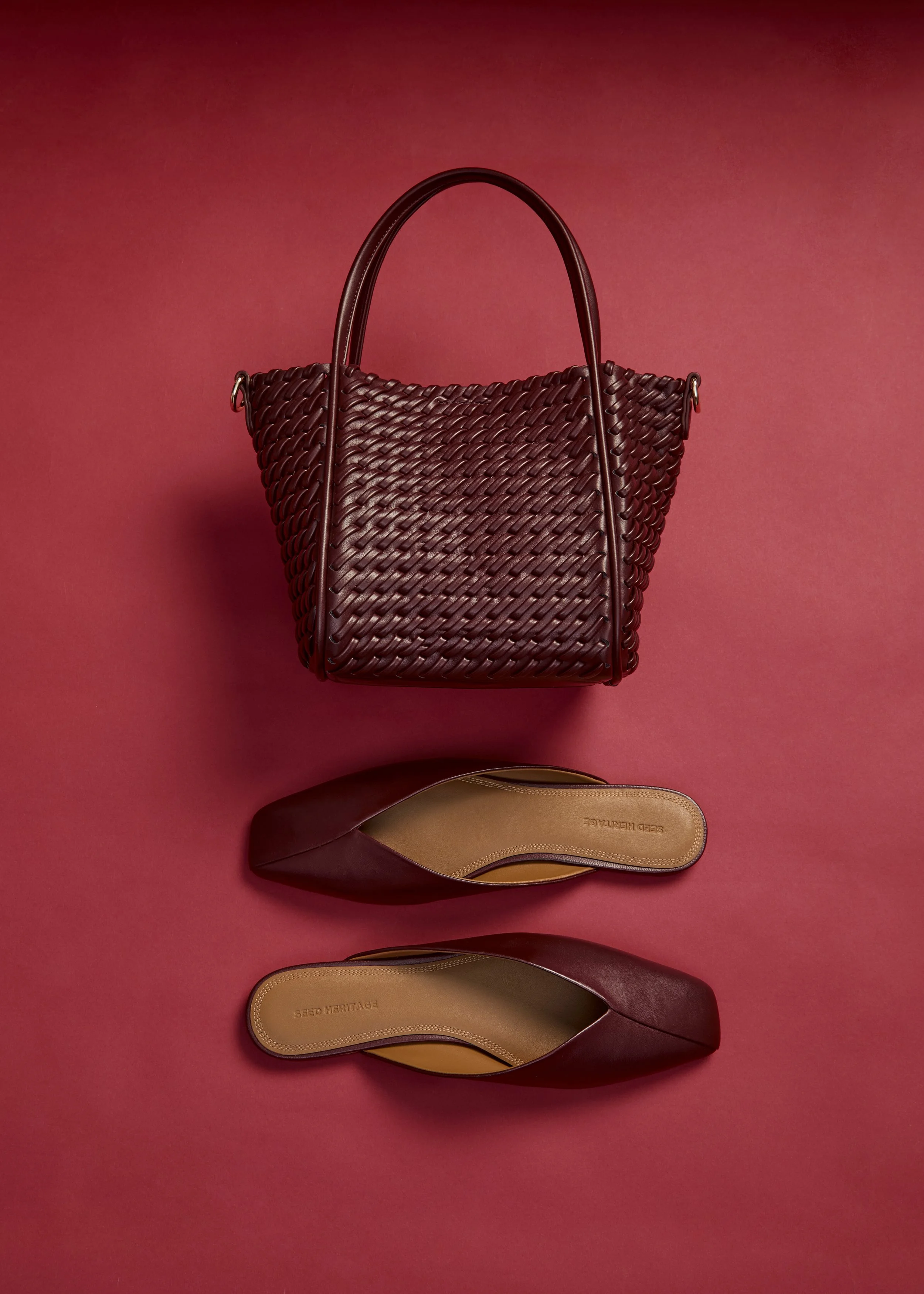 A woven maroon handbag and a pair of maroon pointed-toe flats on a pink background.