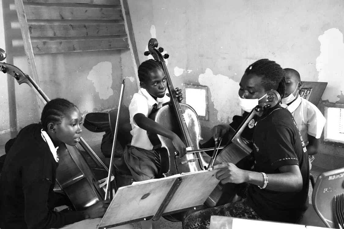 Children playing string instruments in a music class, with some wearing face masks.