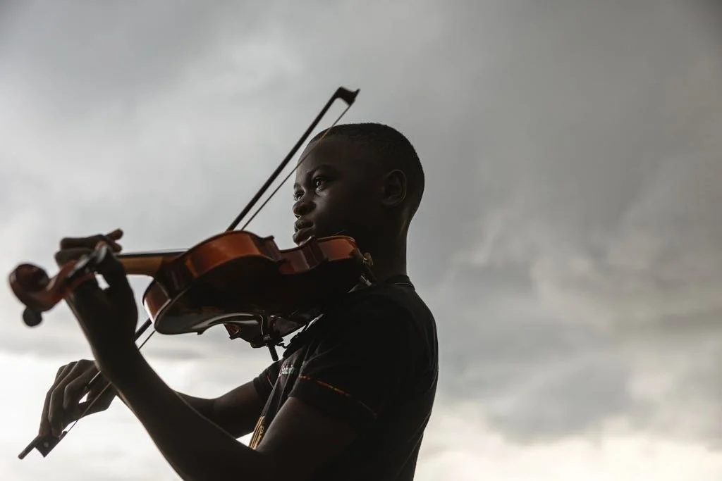 A boy playing a violin outdoors under cloudy skies.