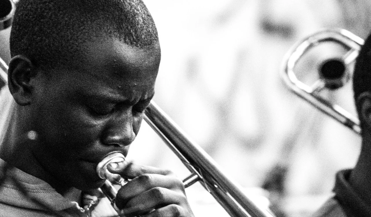 A young man playing a trombone, with a focused expression on his face, in black and white.