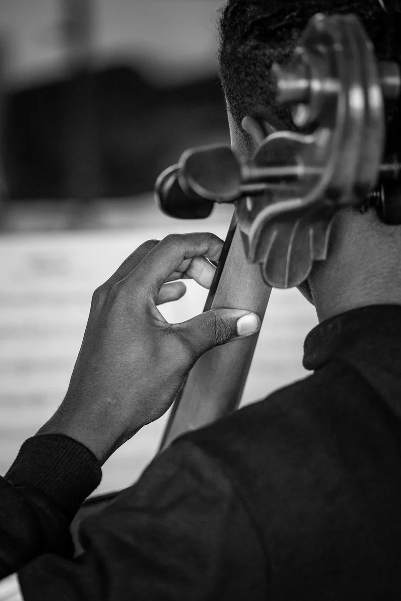 A person with short hair is holding a cello neck and fingerboard, preparing to play or practice.