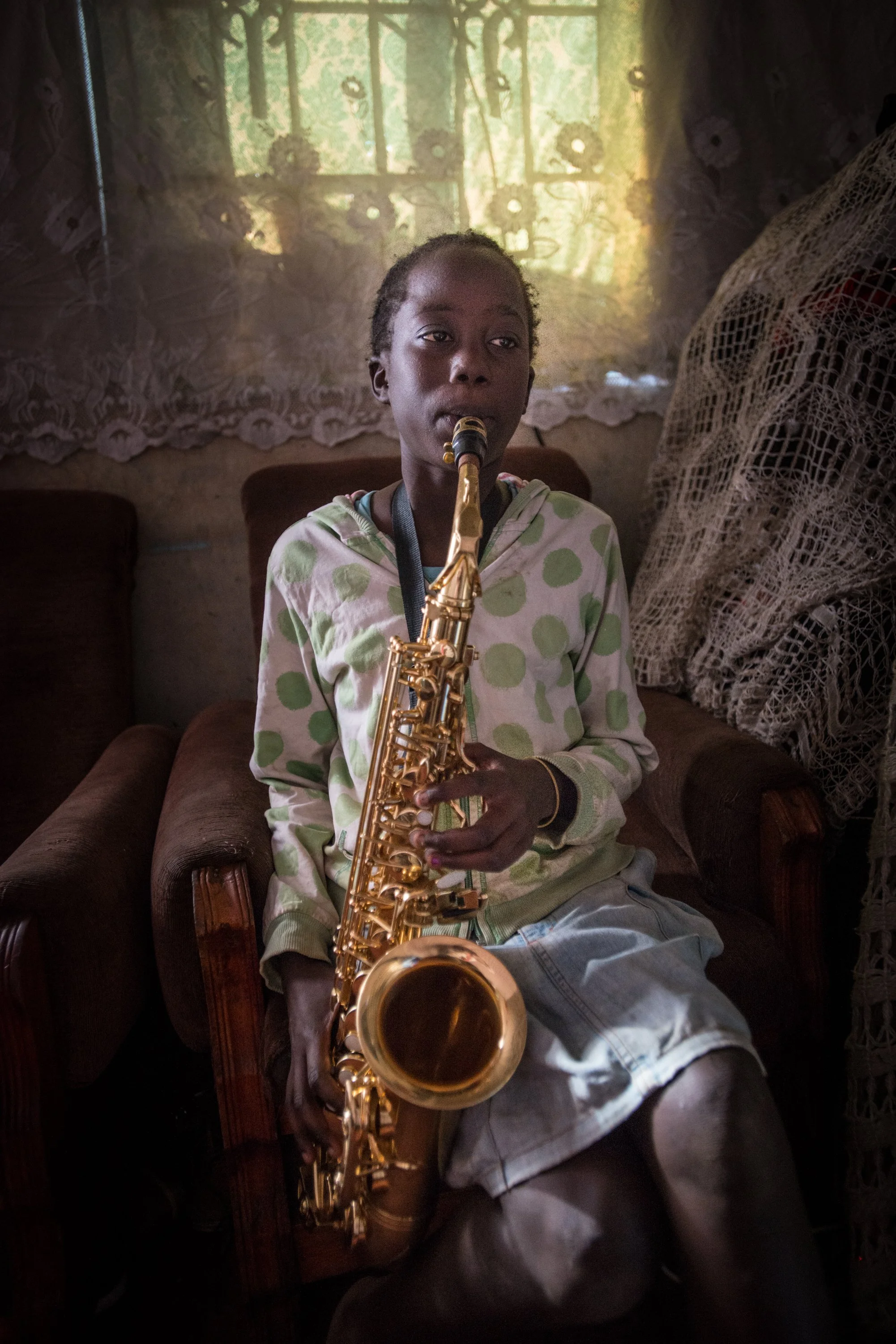 A young person sitting on a chair playing a saxophone.