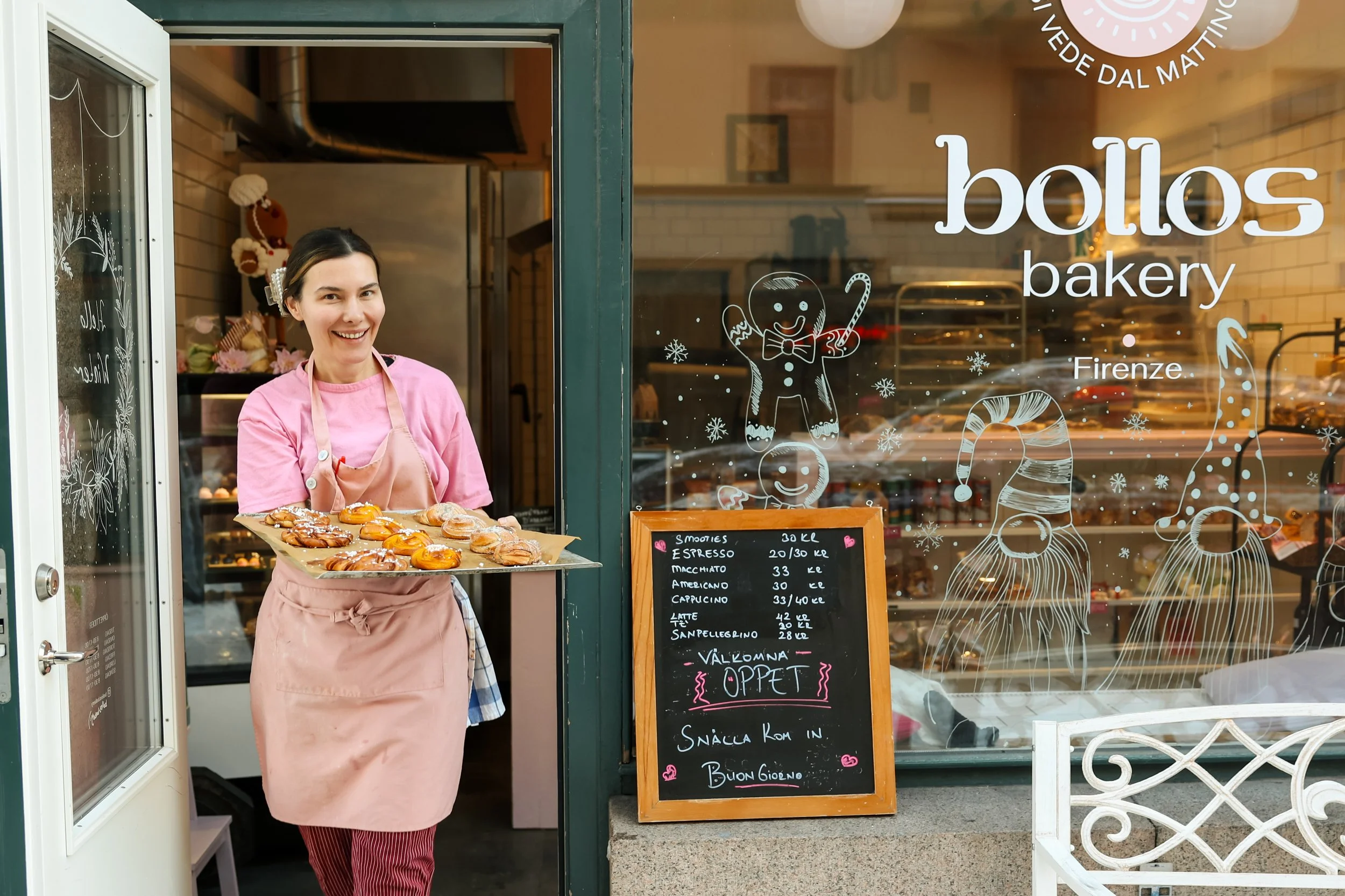 Kvinna som kommer ut från ett bageri med en plåt fylld med kanelbullar