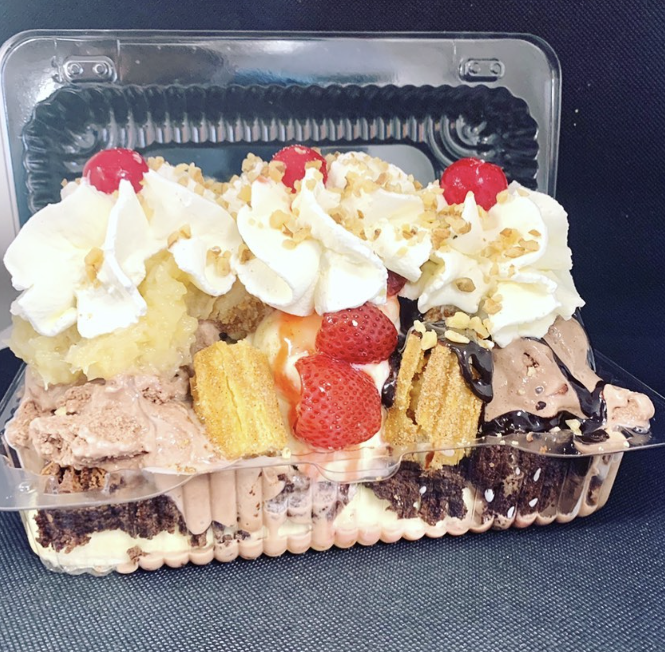 A plastic container filled with various slices and pieces of cake, decorated with strawberries, whipped cream, and chopped nuts.