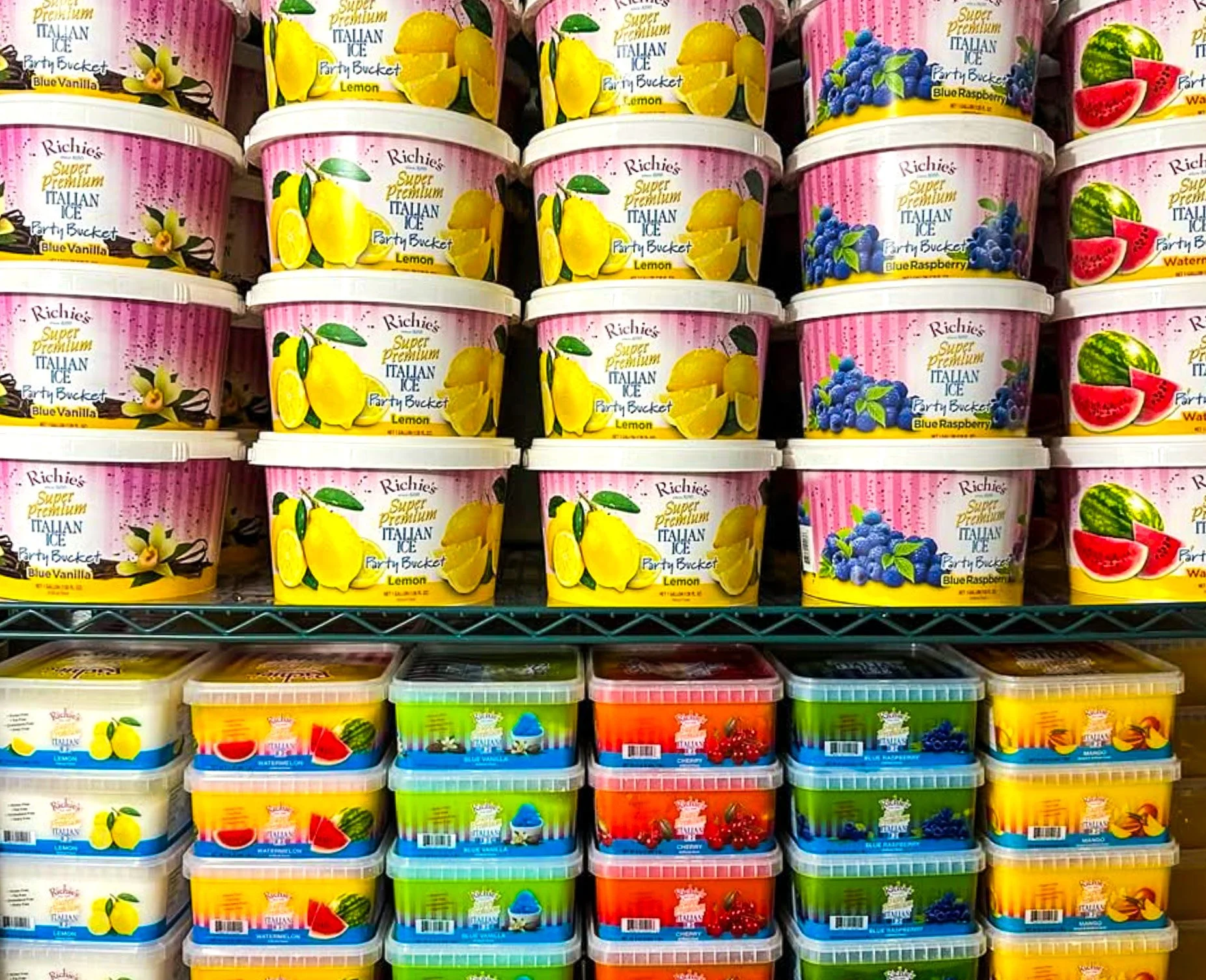 Multiple containers of Richie's Italian Ice flavors on store shelves, including Lemon, Blue Raspberry, Watermelon, Cherry, Blue Vanilla, and Mango, arranged in rows.