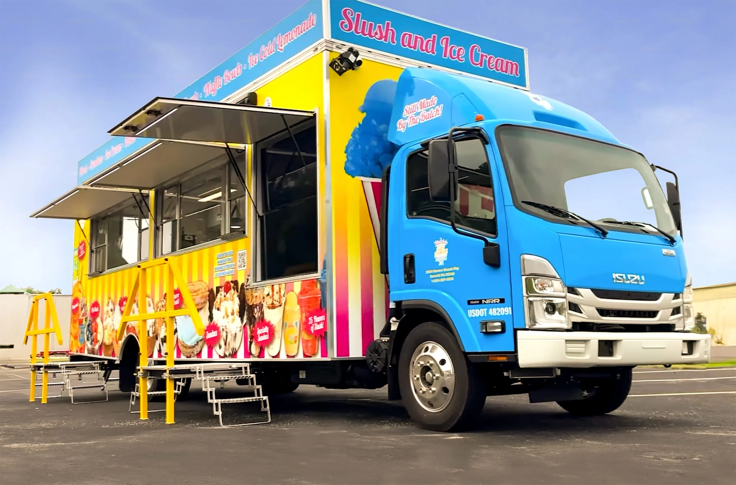 A vibrant blue food truck with a yellow and pink design, advertising slush and ice cream. The truck features large windows, an awning, and steps for ordering, parked on an empty lot under a clear sky.